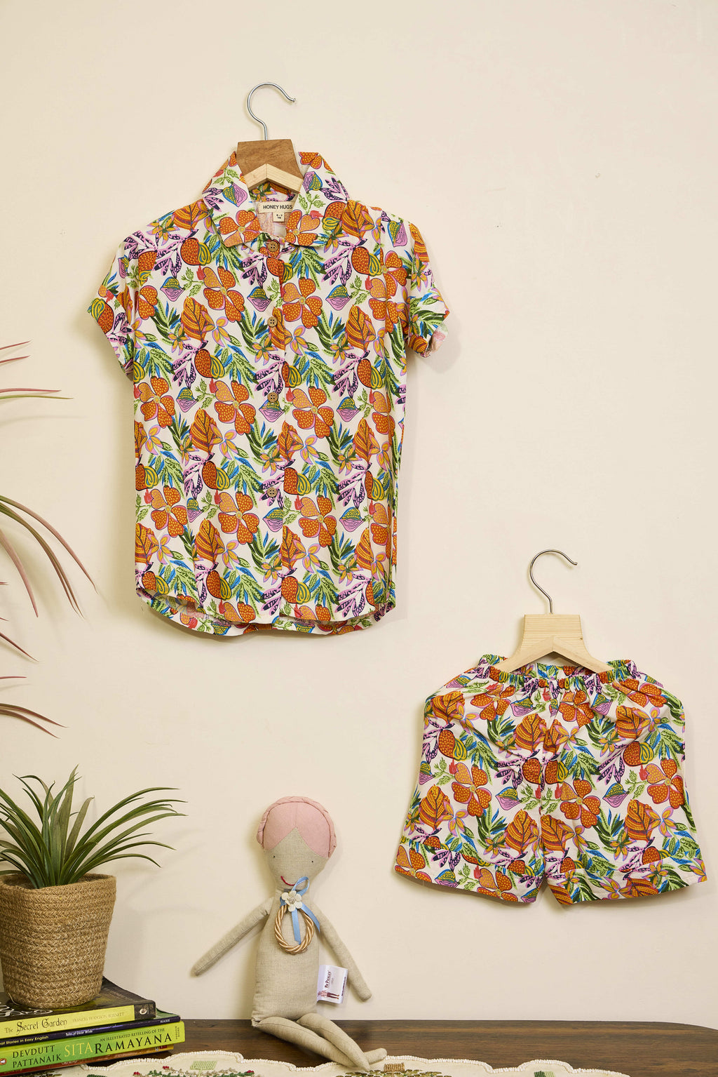 Floral shirt and skirt set on hangers against a beige wall with a plant and books in the foreground.