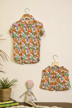 Floral shirt and skirt set on hangers against a beige wall with a plant and books in the foreground.