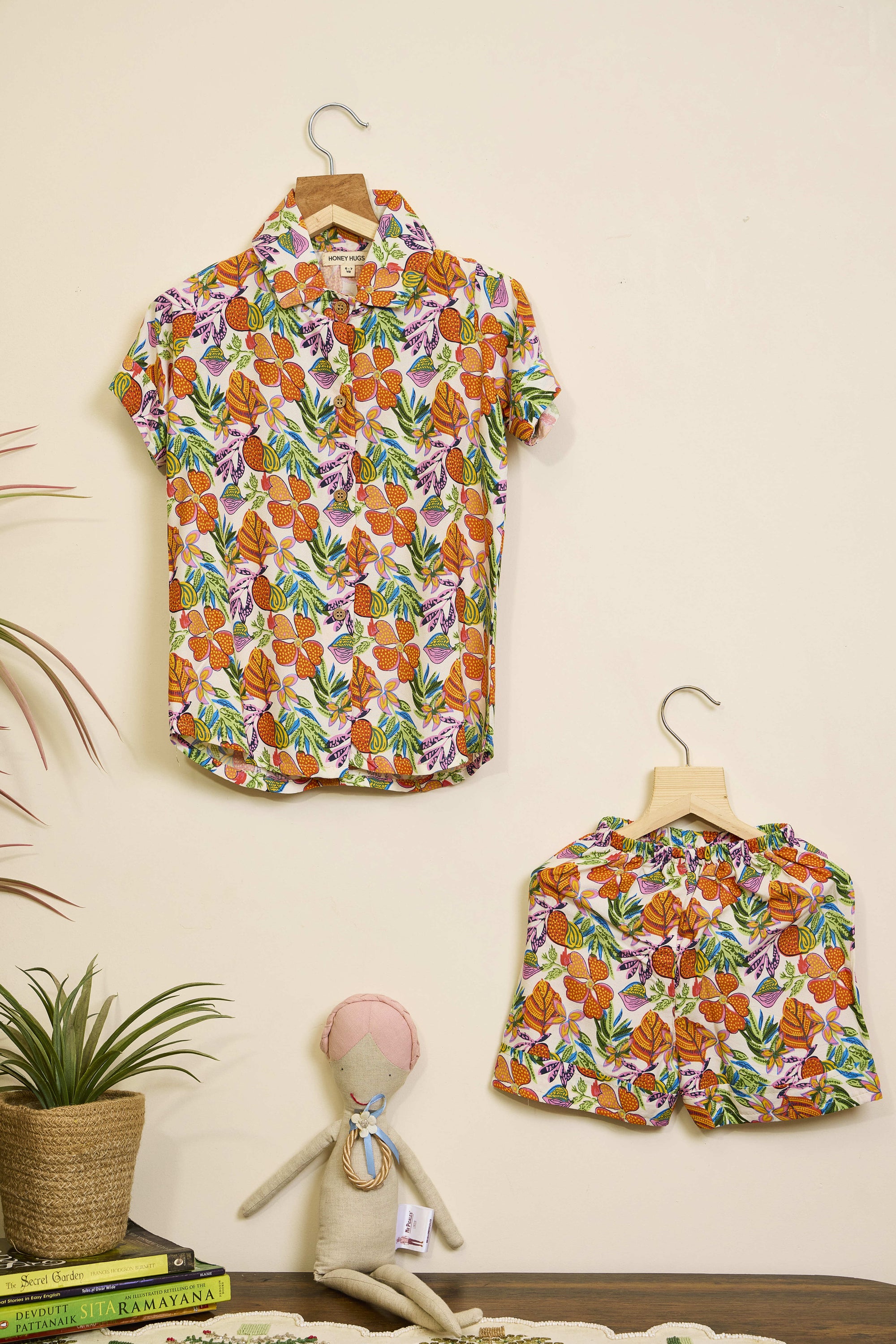 Floral shirt and skirt set on hangers against a beige wall with a plant and books in the foreground.