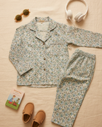 Floral pajama set with slippers, sunglasses, and headphones on a beige surface