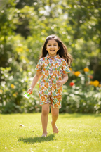 Young girl in a floral outfit standing on grass with a blurred green background
