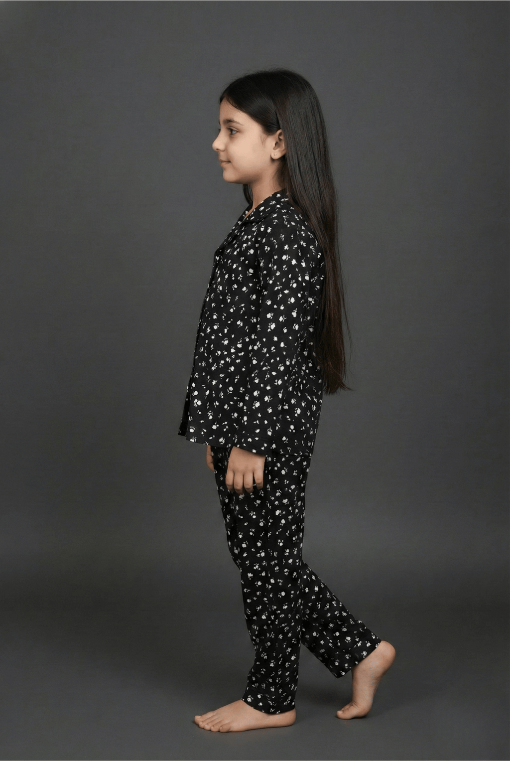 Young girl wearing a black pajama set with white patterns on a gray background