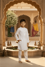 Young boy in a white traditional outfit standing in front of an ornate archway with decorative elements.