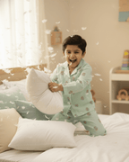 Child in pajamas playing with pillows on a bed in a bright room