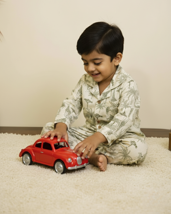 Young boy in printed cotton pajamas playing with a red toy car while sitting on a soft rug.