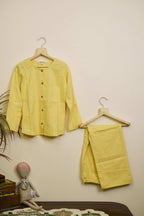 Yellow shirt and pants on hangers against a beige wall with a small plant and toy in the foreground.