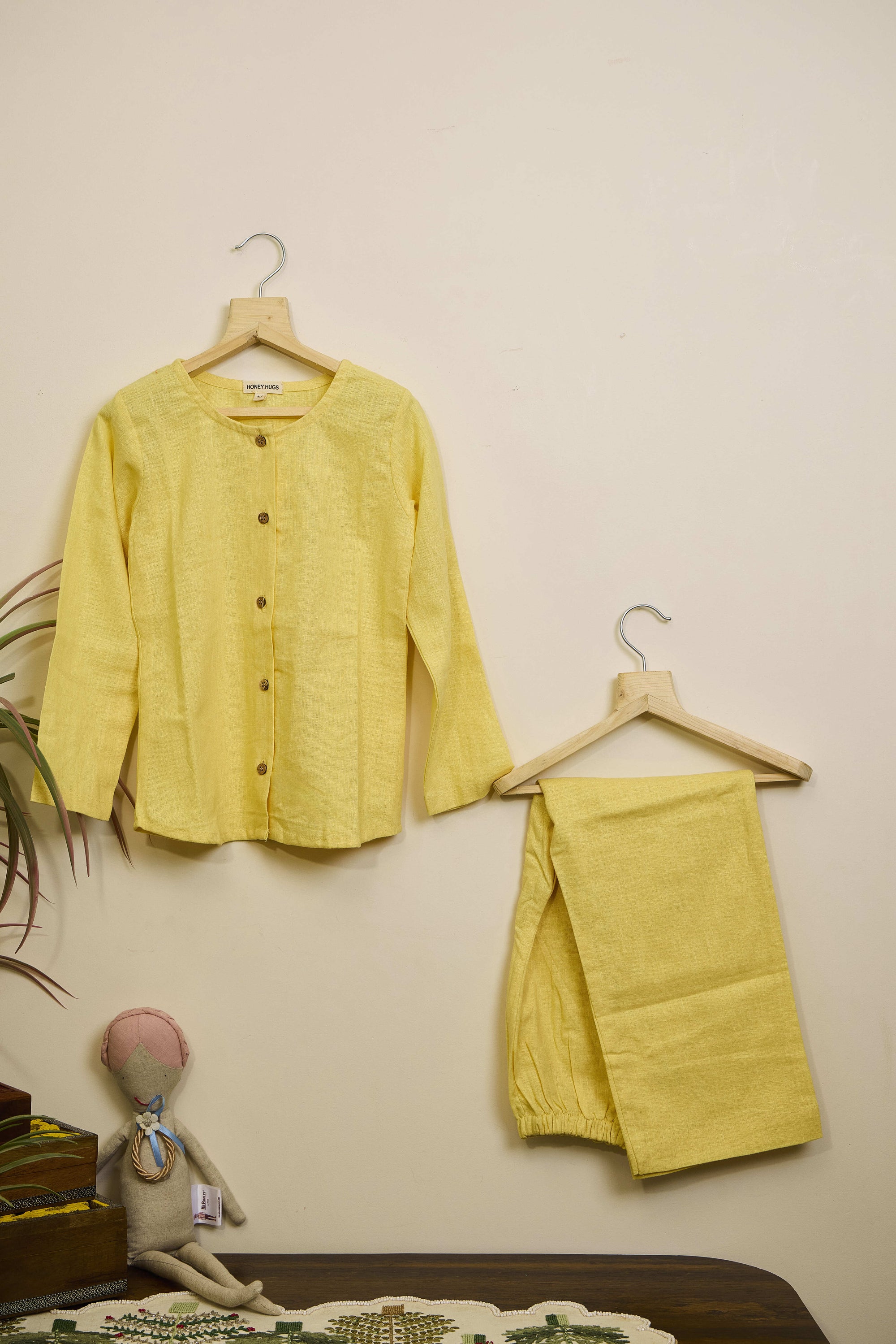 Yellow shirt and pants on hangers against a beige wall with a small plant and toy in the foreground.
